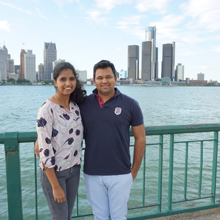 Two people posing at riverfront, Detroit in background