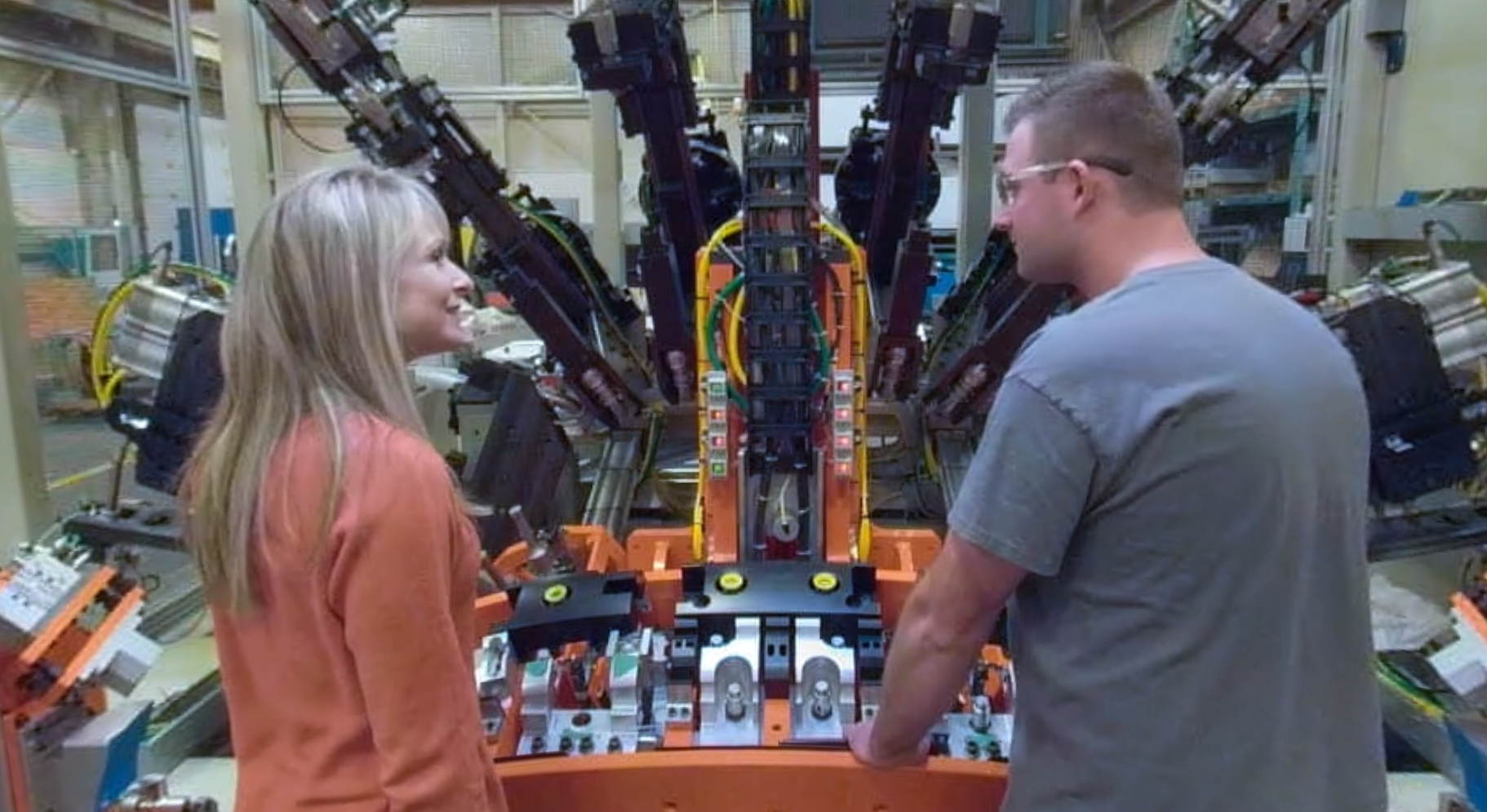 Two people in front of machinery at a manufacturing facility
