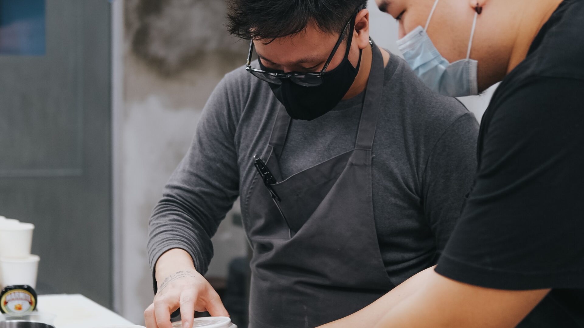 Two men in medical masks preparing food in a restaurant kitchen